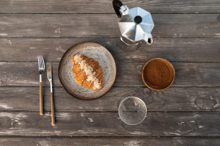 A Croissant on a Plate beside a Moka Pot